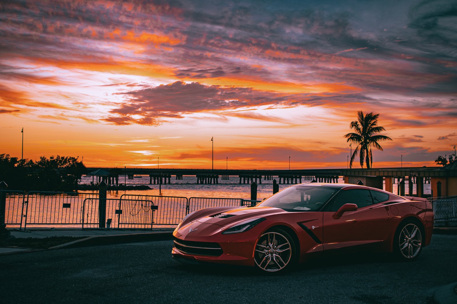 Red Corvette Stingray with dramatic pink and orange sunset sky over Florida coast