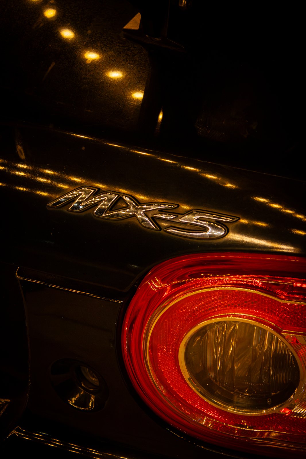 Mazda emblem close-up with string light bokeh reflections — premium detail photography