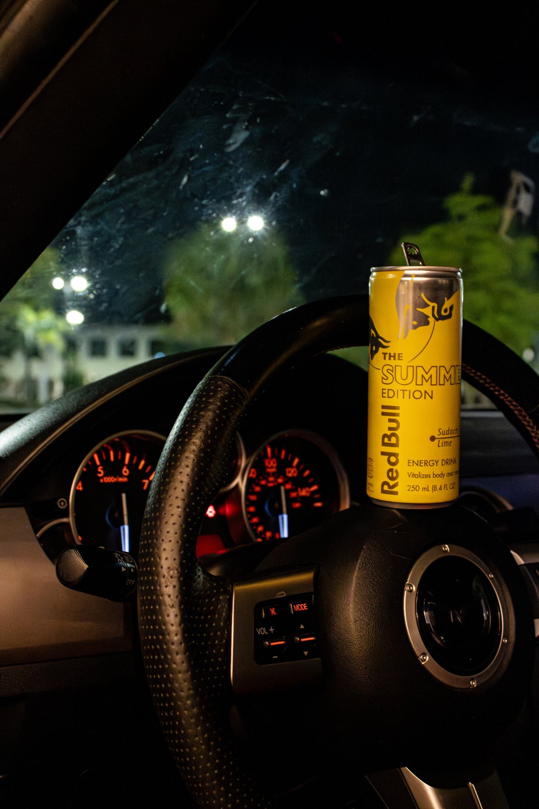 Red Bull can on Mazda MX-5 steering wheel with red gauge cluster glowing — interior automotive photography