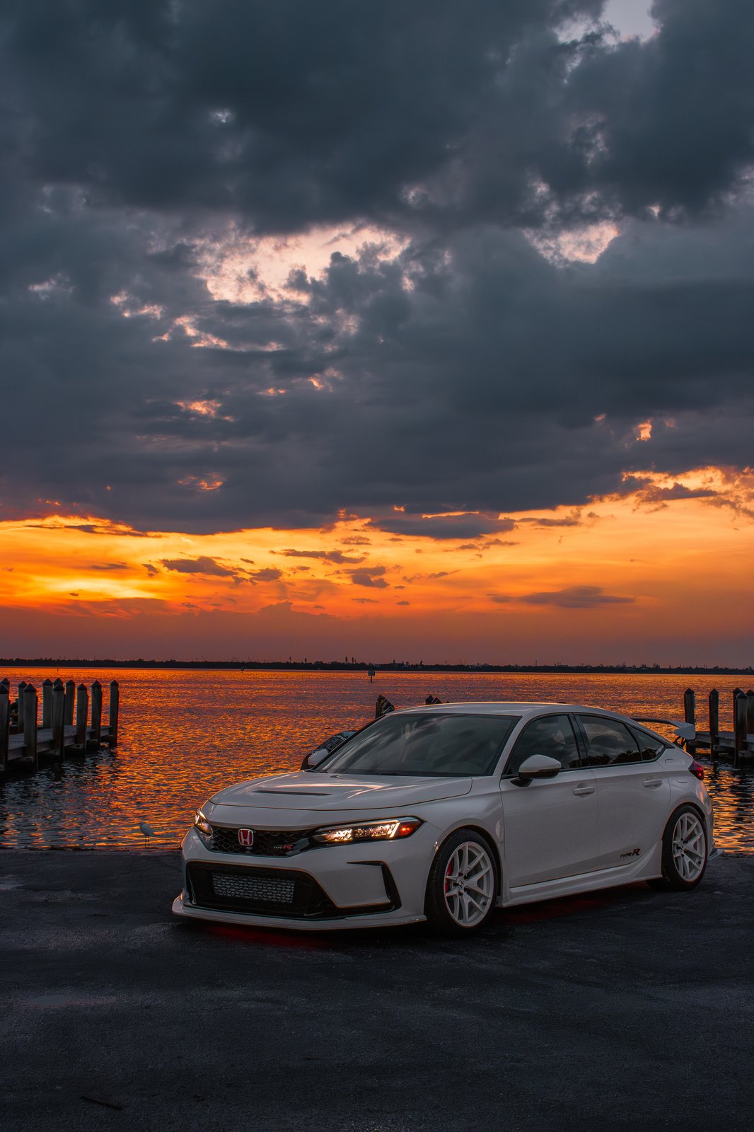 White Honda Civic Type R three-quarter view with dramatic sunset clouds over the water
