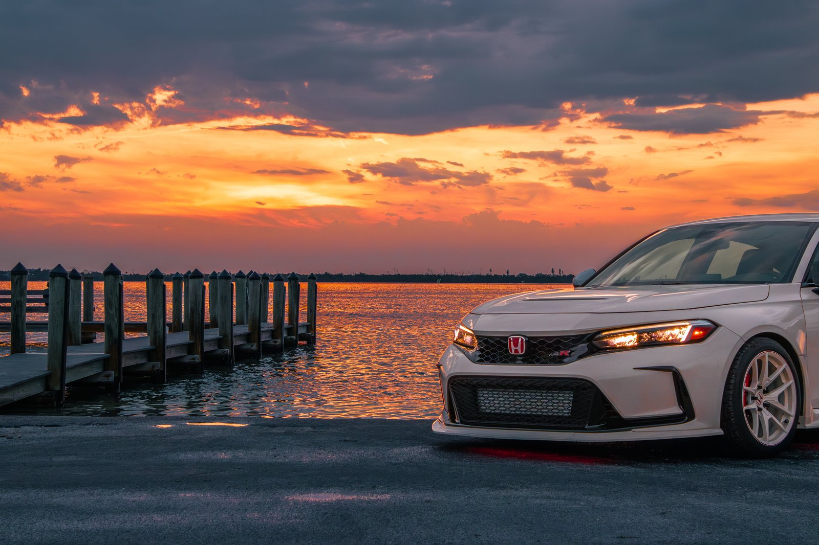 Honda Civic Type R front-end portrait against vibrant orange sunset clouds and water reflection